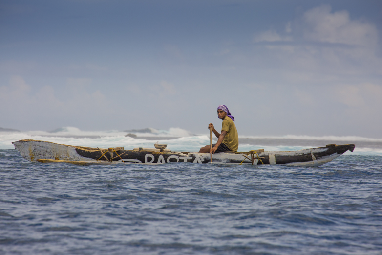 Locals in dugout canoes ride the swell while divers are in the water collecting various fish and edibles. In an hand-to-mouth economy, the ocean provides much of the island with food.
