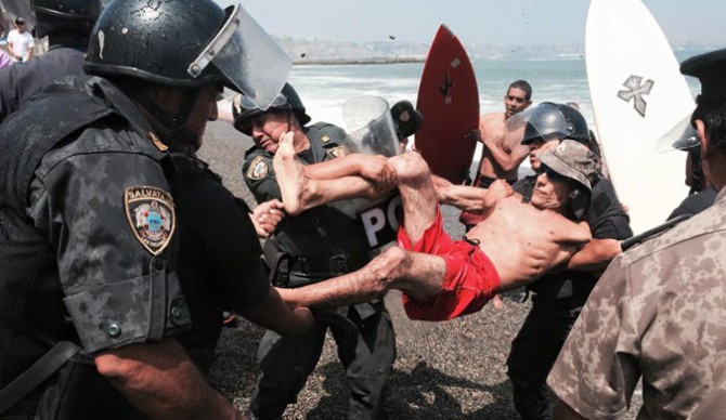 Surfers clash with riot police over a beach being destroyed to protect a roadway.