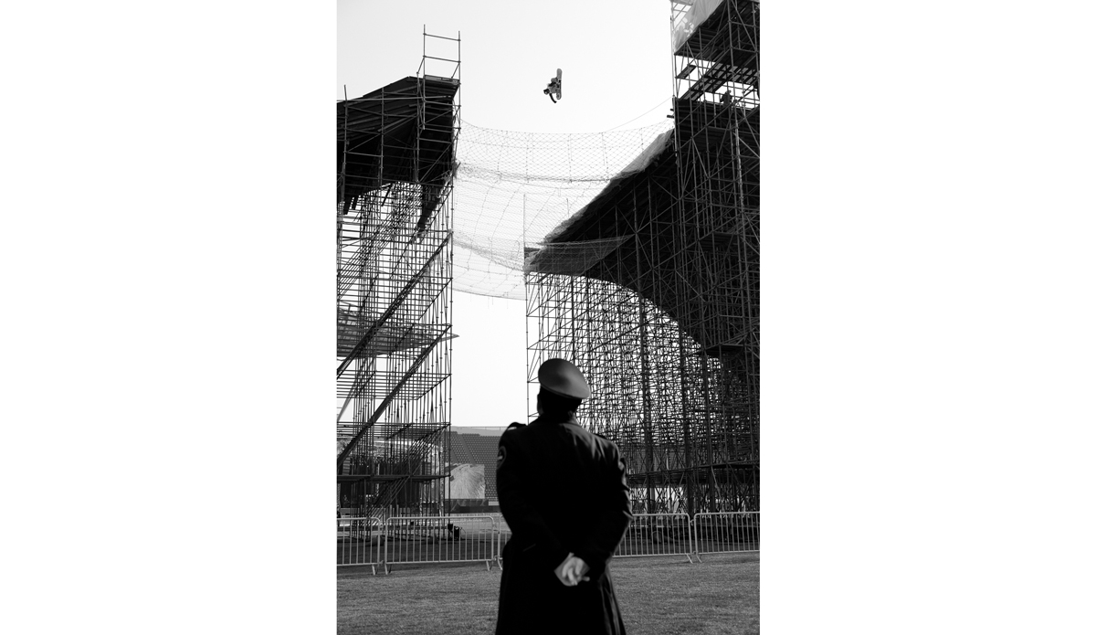 Mark McMorris being watched closely by a Chinese military officer during the practice session for the Air and Style Beijing.  Snowboarding in stadiums is always sort of strange, but add military all over the place, and the fact that you are in Beijing, its just got awkward. Photo: <a href=\"https://www.adammoran.com/\">Adam Moran</a>