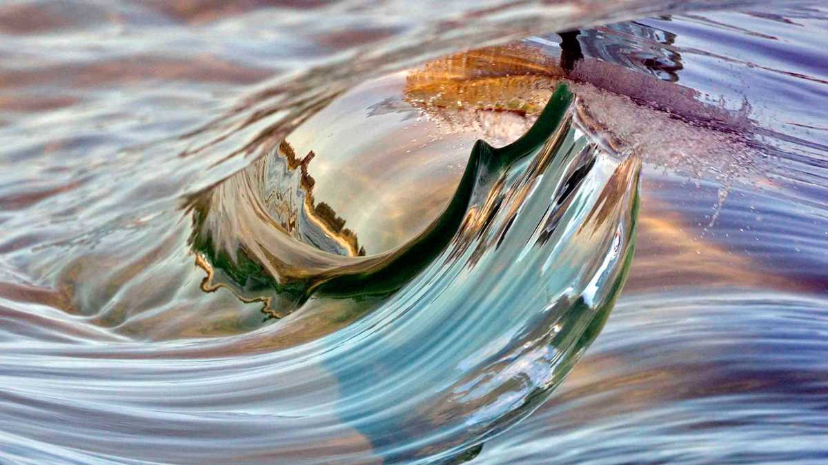 Ok, so sometimes you just need to look at something differently to see a alternative prospective, this is the case with this image with the reflection of the shoreline captured in the hollow of the wave. Photo: <a href=\"https://debmwaveart.webs.com/\">Deb Morris</a>
