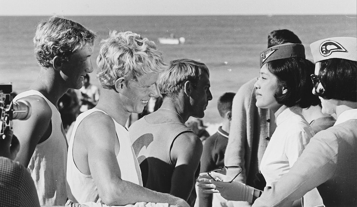 Even surfers in ’64 had groupies. Midget Farrelly and Nat Young mingle with the fans at the historic inaugural World Surfing Championship held at Manly Beach, Australia. The contest was significant in that it was the first time in history that all of the world’s surfing countries came together and competed against one another in a sanctioned, sponsored forum. Photo: <a href=\"https://www.isasurf.org/\">Jack Eden | ISA</a>