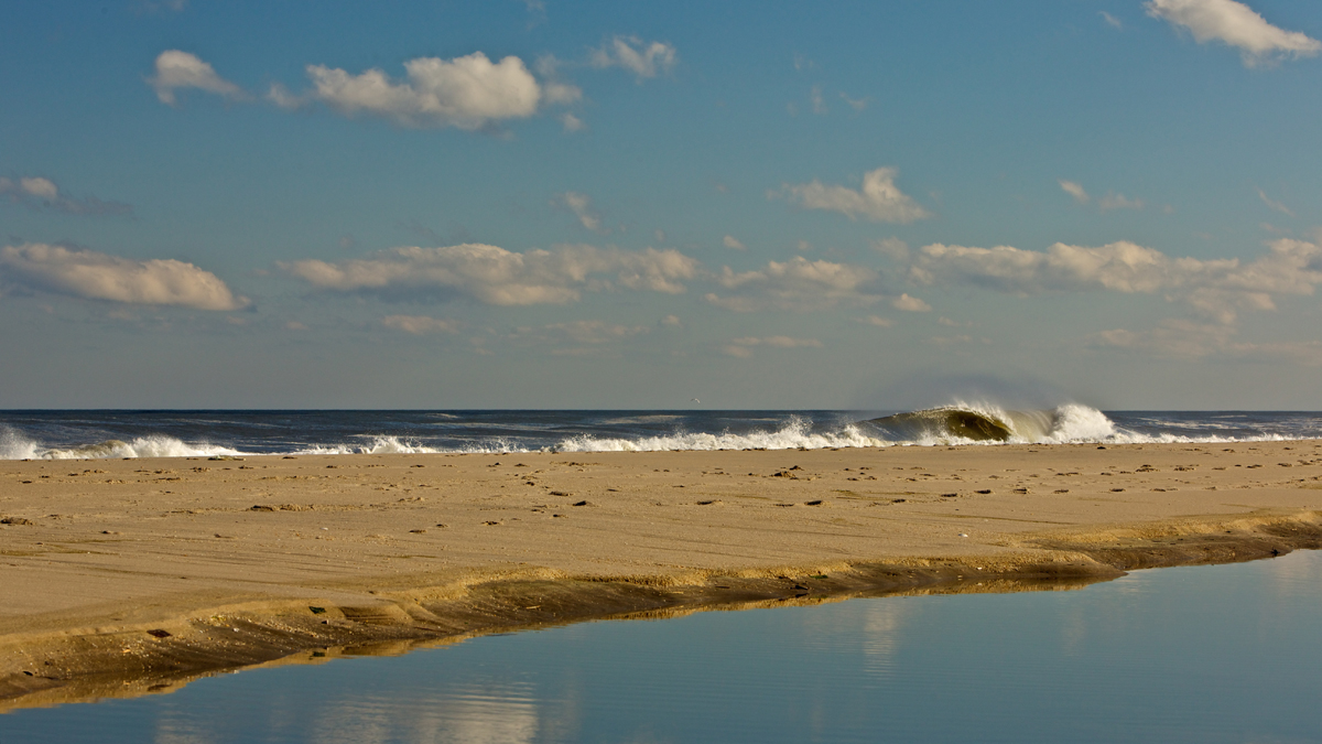 An ocean pool, left like a sheet of glass from high-tide, casting a reflection of the sky. I just had to wait for that right one to grind along the sand bar to make it work.