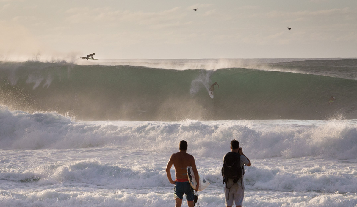 A surfer bails out as another drops in in front of spectators and drones.