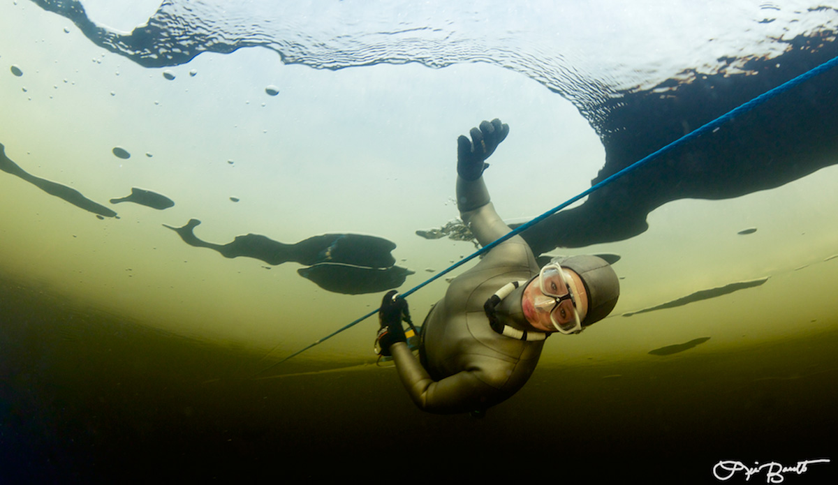 Freediver Chloe Villaume pauses between ice holes. Photo: <a href=\"https://liabarrettphotography.com/\" target=_blank>Lia Barrett</a>