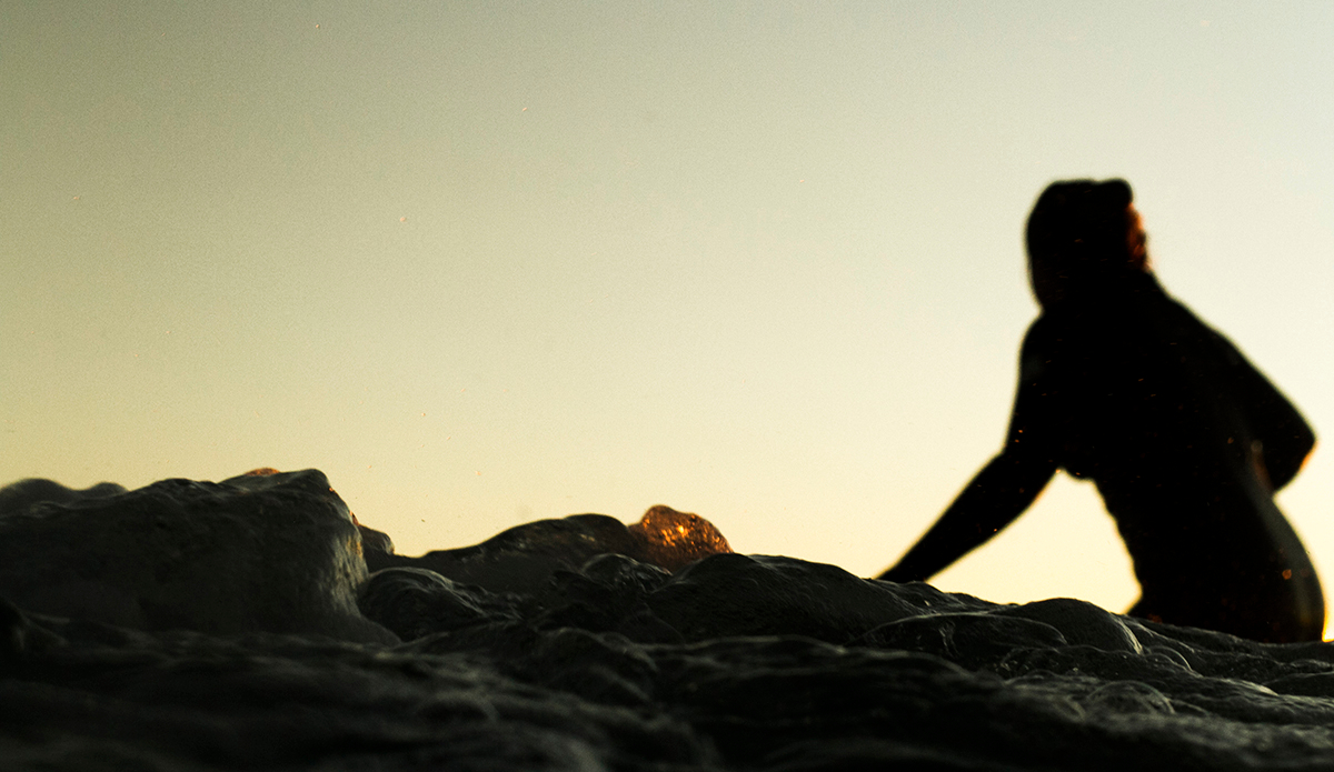 Chelsea Williams—Rainbow Bay, Australia.
There is no surfer more difficult to photograph than Chelsea Williams. And not because she isn’t one of the most skilled longboarders in the world. I had unsuccessfully arranged to photograph Chelsea on more than a handful of occasions before this day, but finally locked her down on this winter afternoon. The photo is a complete representation of Chelsea. Camera shy as she surfs away from the lens and avoiding attention, not wanting to be the focus of the shot. The darkness in the image rings true to her affectionate nickname \"Hellsea.\" But the spot of fire of light that illuminates the centre water bubble in the image is the eternal burning desire that fuels Chelsea’s surfing and allowed her after a decade of heartbreak, to win her world title. Photo: <a>Fran Miller</a>
