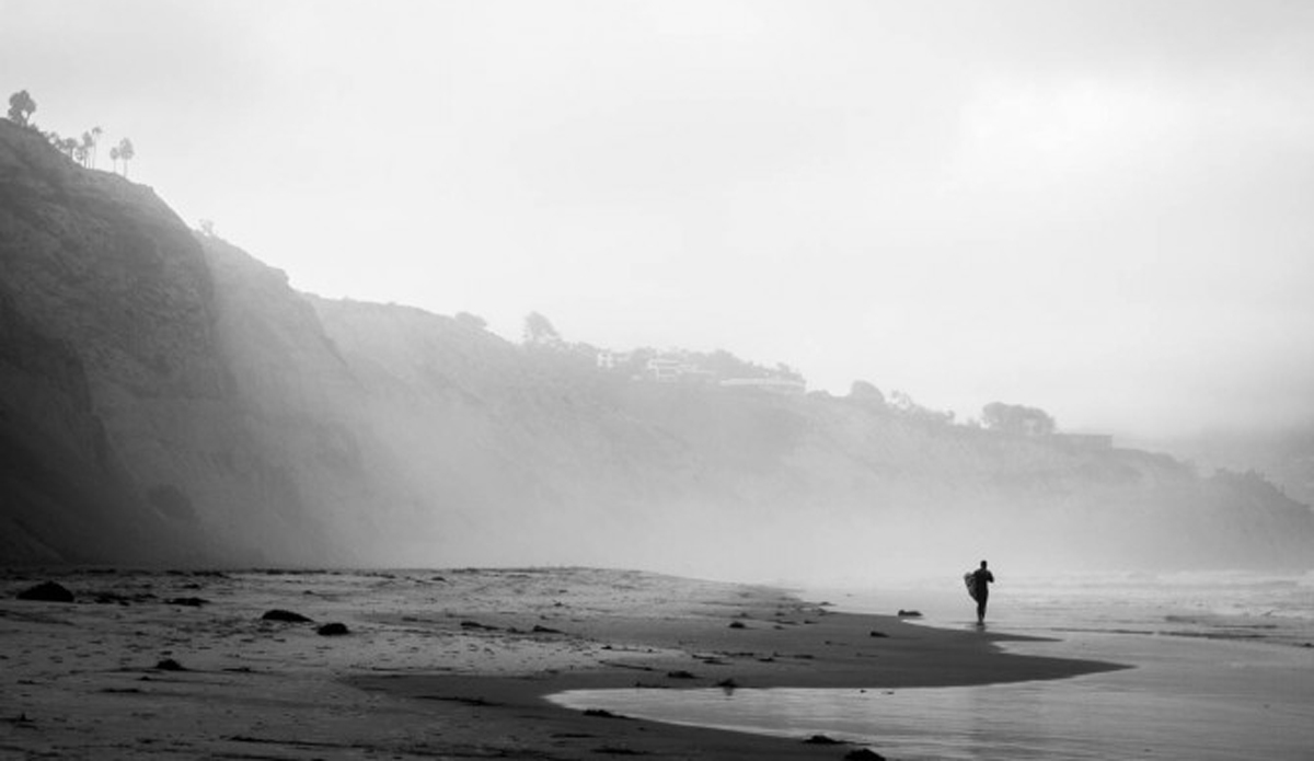 An unknown surfer making the morning walk to the beach front.