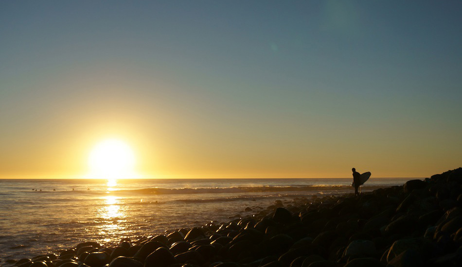 A local surfer contemplates bare foot placement on urchin-covered cobblestones under a Mexican sunset. Photo: <a href=\"https://www.milesjackler.com\">Miles Jackler</a>