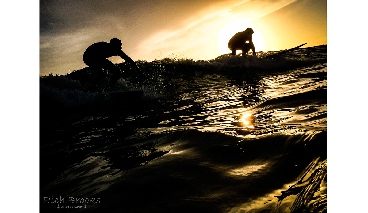 Two surfers perfectly silhouetted against the sun. Photo: <a href=\"https://richbrooksphotography.squarespace.com/\">Rich Brooks</a>