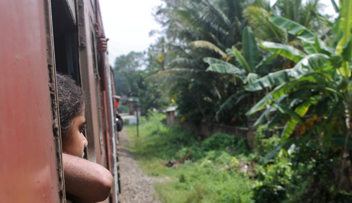 A young girl enjoys the views from the train that takes you along the west coast of Sri Lanka. The trip is filled with views of rare wildlife, palm trees, and stunning beaches.  Photo: <a href=\"https://www.ryanwattersphoto.com/\">Ryan Watters</a>