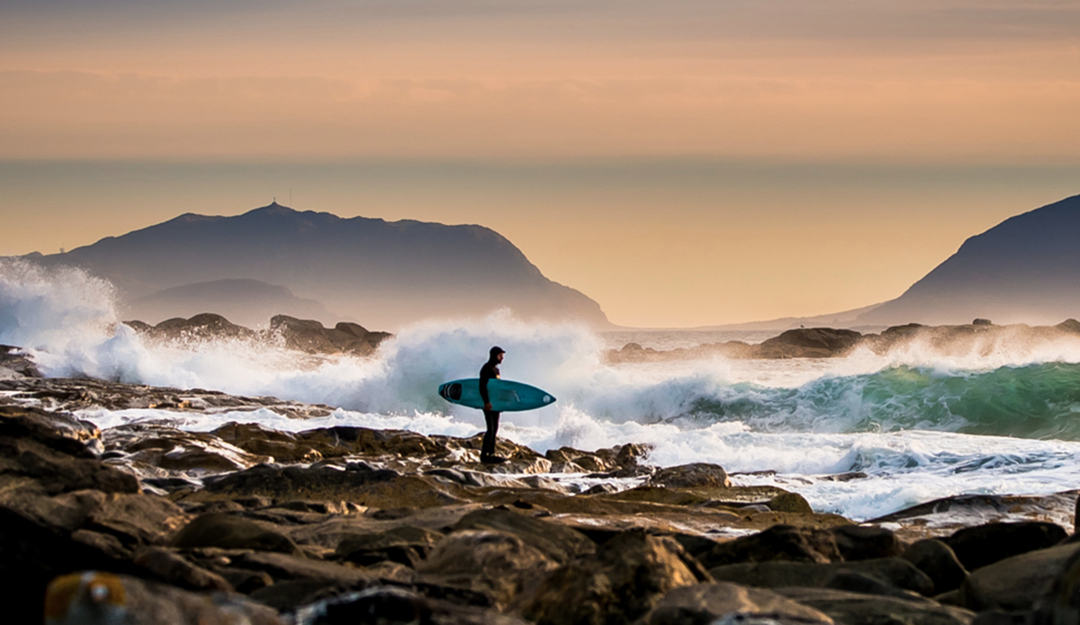 I visit an old friend, who lives with mountains by the sea. For him there was a reason moving here, to the west coast of Norway, and an idea of exploration and documentation. It is an endless conversation with a landscape of snowy mountains, deep fjords, wild sea, strong winds, dark forests, rainy days and aurora nights. The work never stops as long as time is changing. And on an island, on an empty beach, cold surfing is on. Weather and temperature waits for no one. Photo: <a href=\"https://www.fjordlapsephotography.com/\">Fjordlapse Photography</a>
