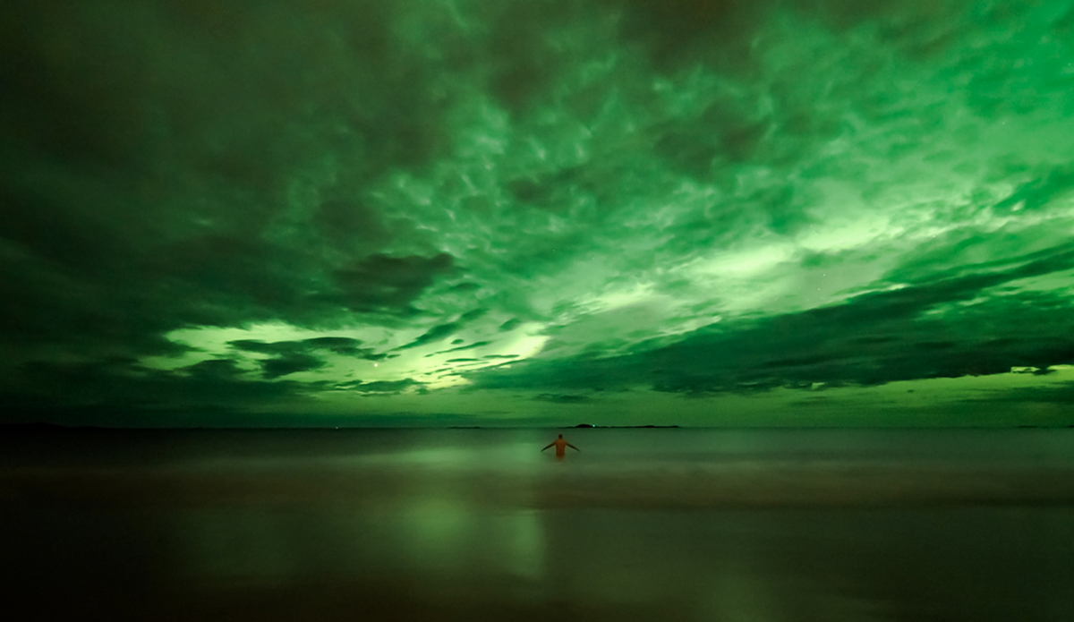 Images haunt us.
The car rumbles down with headlights cutting through thick darkness following the dirt road. Unseen matters outside, we stop the car looking at light green standing sticks ripping the sky.
A white beach in the night, heavy blue clouds and northern lights, dancing in front of our cameras. Naked and the sea.
We haunt for images. Photo: Photo: <a href=\"https://www.fjordlapsephotography.com/\">Fjordlapse Photography</a>