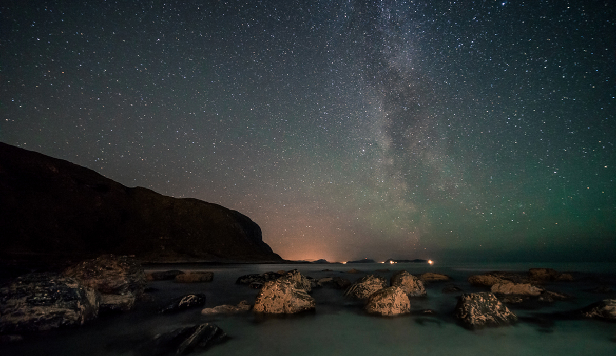 Where do we go?
Someone threw bulky rocks over the side of the bay, like dots against the petrol blue backdrop. Dead kelp on the beach, harvested in the storm. The Milky Way gives directions, throwing its white map over the sky.
Can’t go home yet. A purpose without objective.
Move on. Photo: Photo: <a href=\"https://www.fjordlapsephotography.com/\">Fjordlapse Photography</a>
