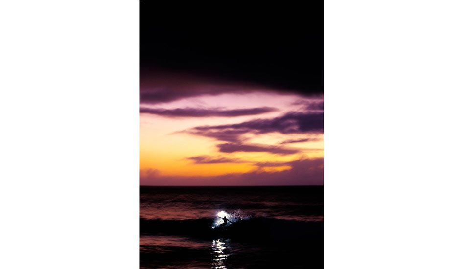 Flash was doing the rounds again via the use of remotes. I was doing some remote flash tests with Jamie O\'Brien in front of his house at Pipe. I got thinking about it, and realized that with such a beautiful sunset being put on by nature, I had to make it the star of the image and so I pulled way back to make Jamie smaller against the expanse of the sunset. The result was beautiful. Photo: <a href=\"https://seandavey.com//\" target=_blank>Sean Davey</a>