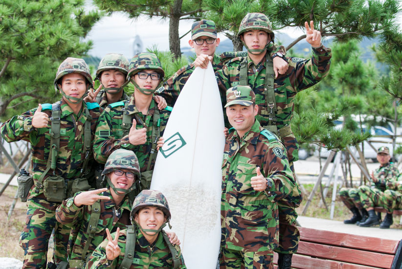 Some young ROK soldiers break the hardship and monotony of their compulsory two year military service defending Korea and grab a chance to pose with my surfboard during a military exercise and a pumping NE swell. I wonder if any of these guys know what a thruster is? Photo: <a href=\"https://www.shannonaston.com/\" target=_blank>Shannon Aston</a>.