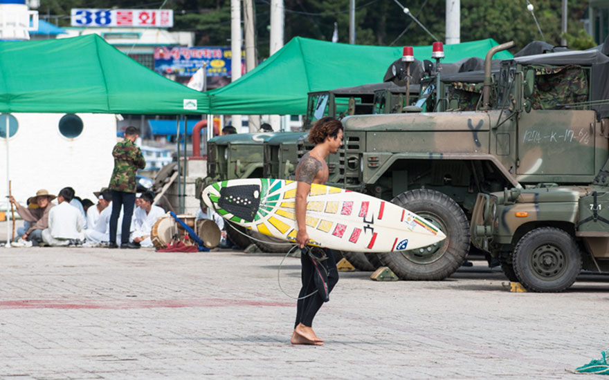 Local surfer Dong-hoon Han heads out through army vehicles during the last typhoon season which brought great waves to the area. Photo: <a href=\"https://www.shannonaston.com/\" target=_blank>Shannon Aston</a>.