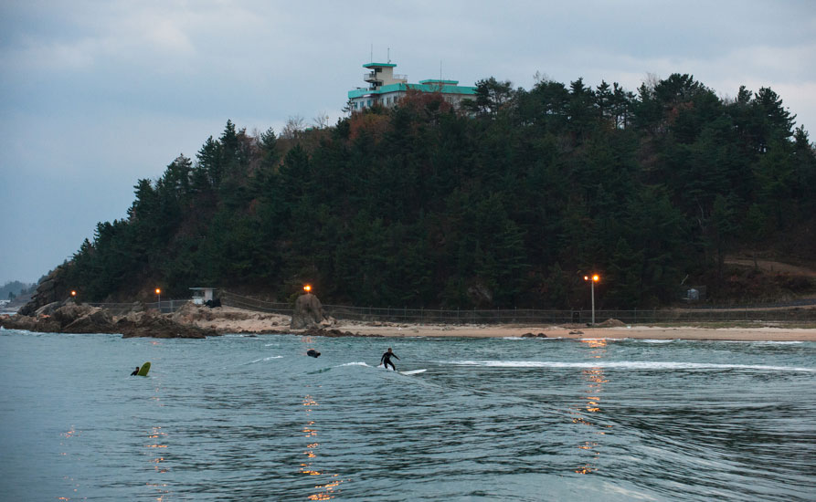 A few longboarders push it right til dark in the fall. The background is framed by barbed-wire fences, military spotlights, and a ROK guard post. Photo: <a href=\"https://www.shannonaston.com/\" target=_blank>Shannon Aston</a>.