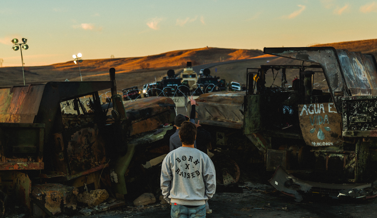 John Hildebrand, staring in the eyes of the over militarized police, armored with middle east conflict style Humvees, automatic weapons, and crowd dispersing sound canons. The police / military presence was there to send a strong signal of intimidation to protestors. Snipers and monitoring vehicles lined the tops of the hills in all directions, and guns were consistently pointed in the direction of the unarmed protestors. However the spirits of the Water Protectors has not been broken or intimidated. Photo: Keegan Gibbs