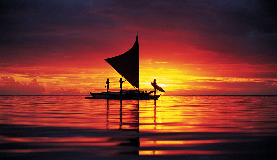 Surfing girls on a traditional sailing outrigger. Bora Bora. Photo: <a href=\"https://www.timmckennaphoto.com/\" target=_blank>Tim McKenna</a>.