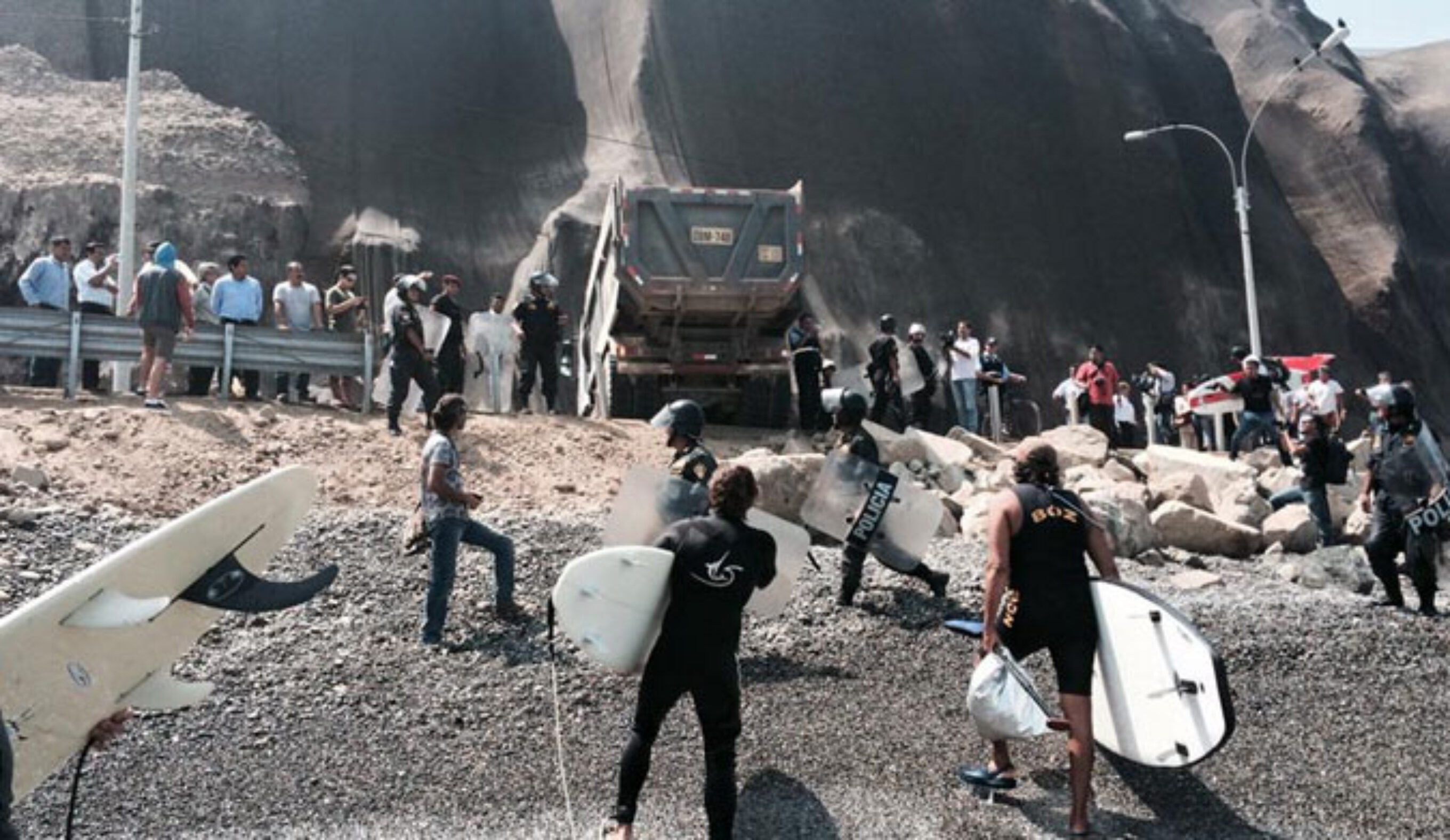 Surfers trying to stop dump trucks from unloading boulders onto the beach. 