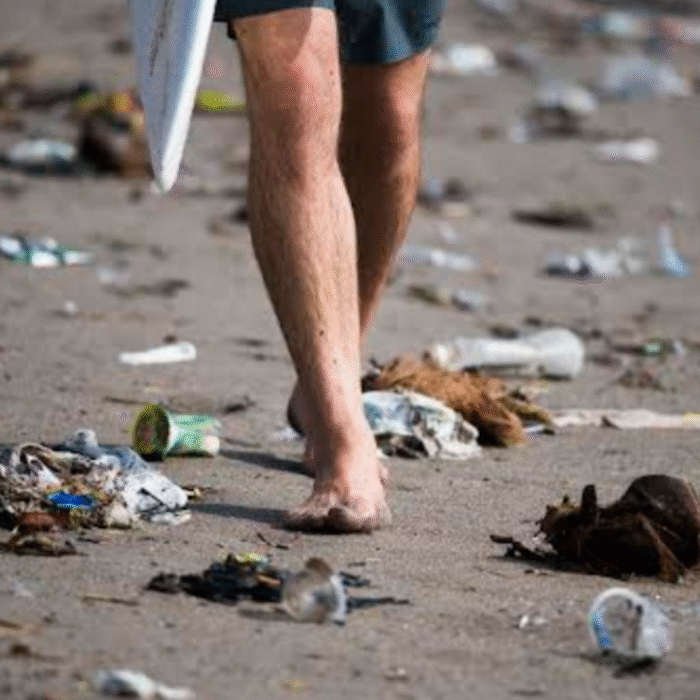 Trash in Bali as surfer walks beach.