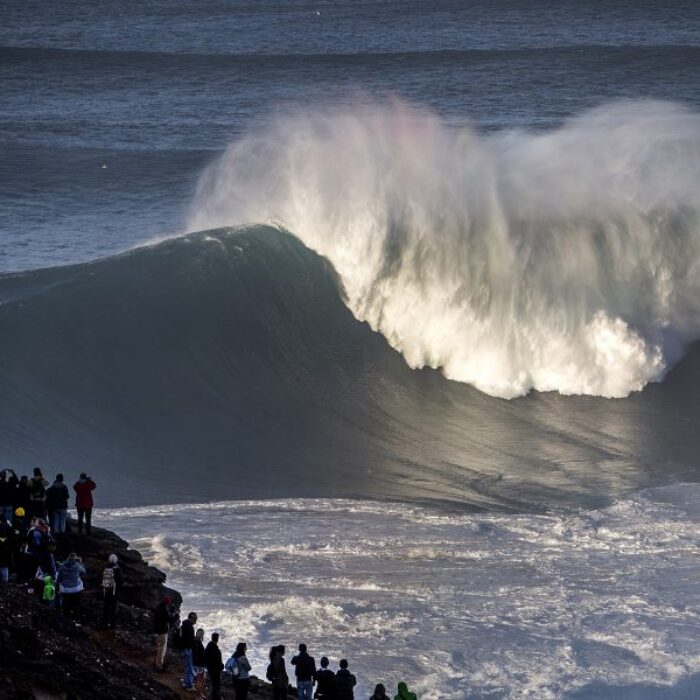 A big wave in Nazare, Portugal with crowds.