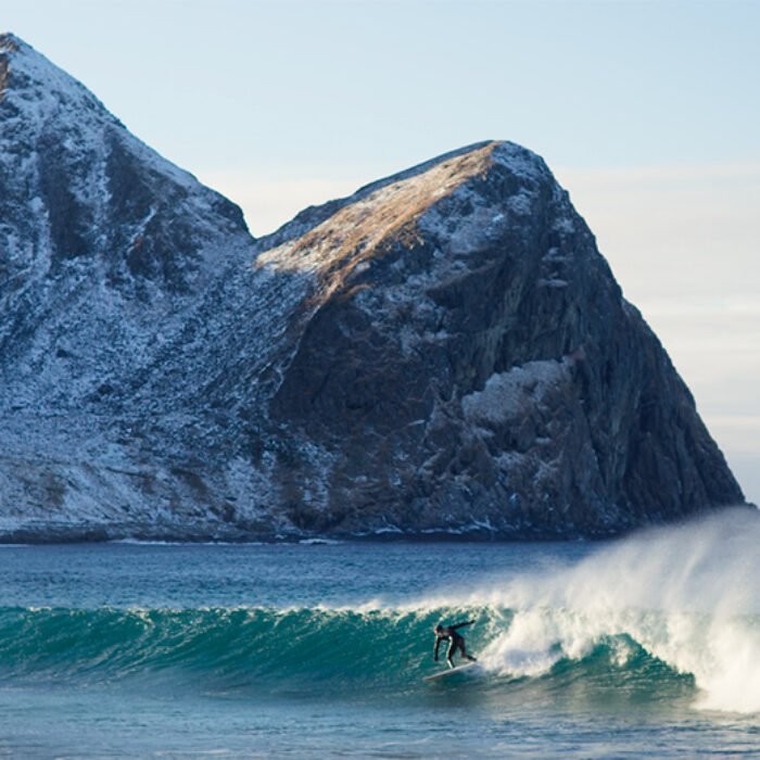 a surfer catches a wave with a snowy mountain behind