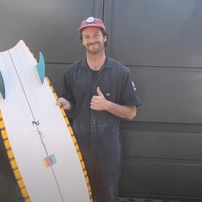 A man holds a twin fin surfboard in front of a van