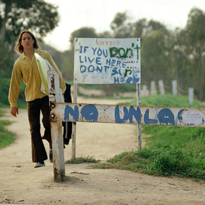 A surfer walks past signs at Sunset Cliffs