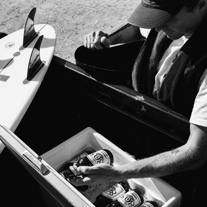 a surfer grabs a beer from the back of his truck