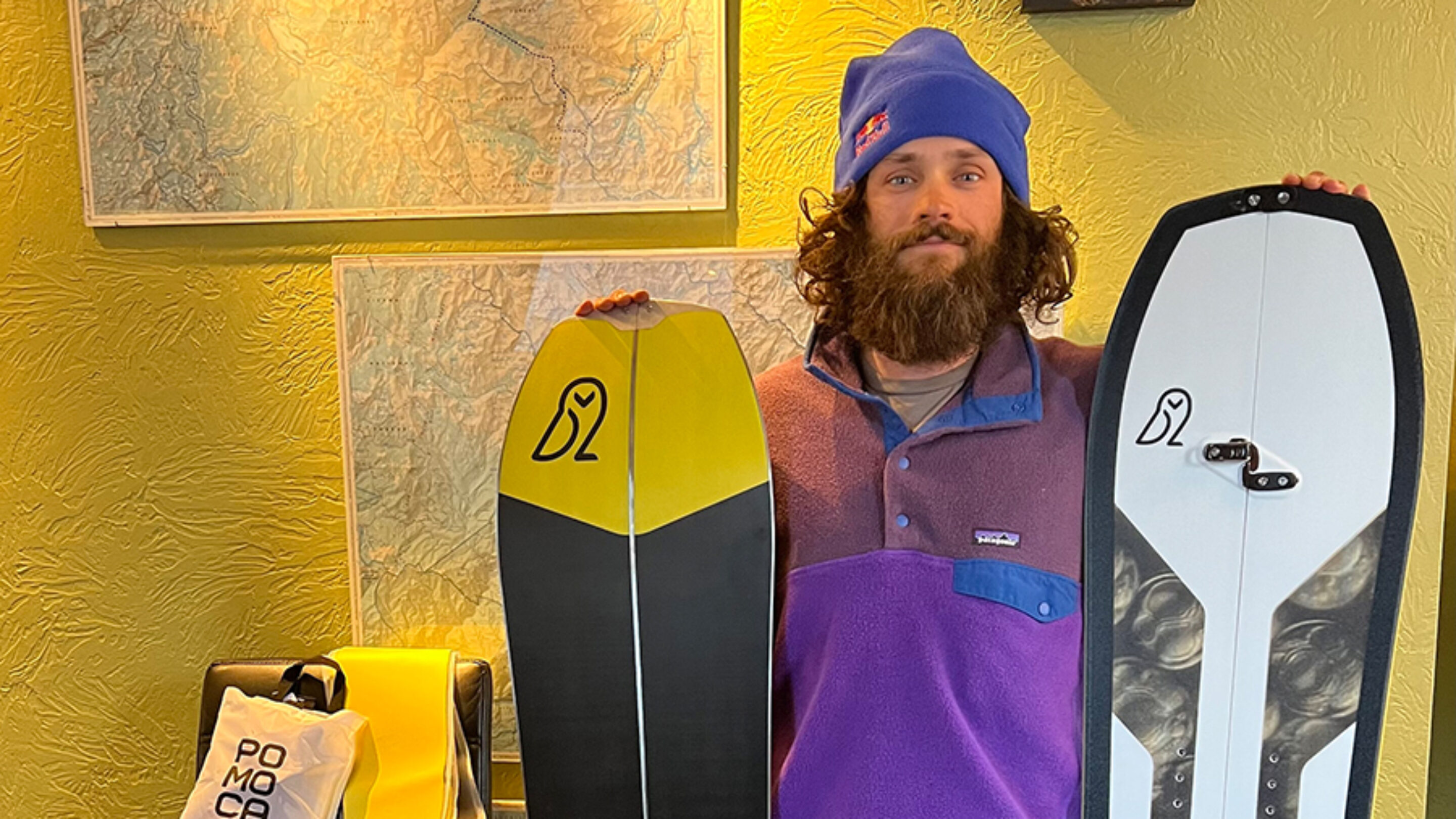 a bearded man holds two snowboards