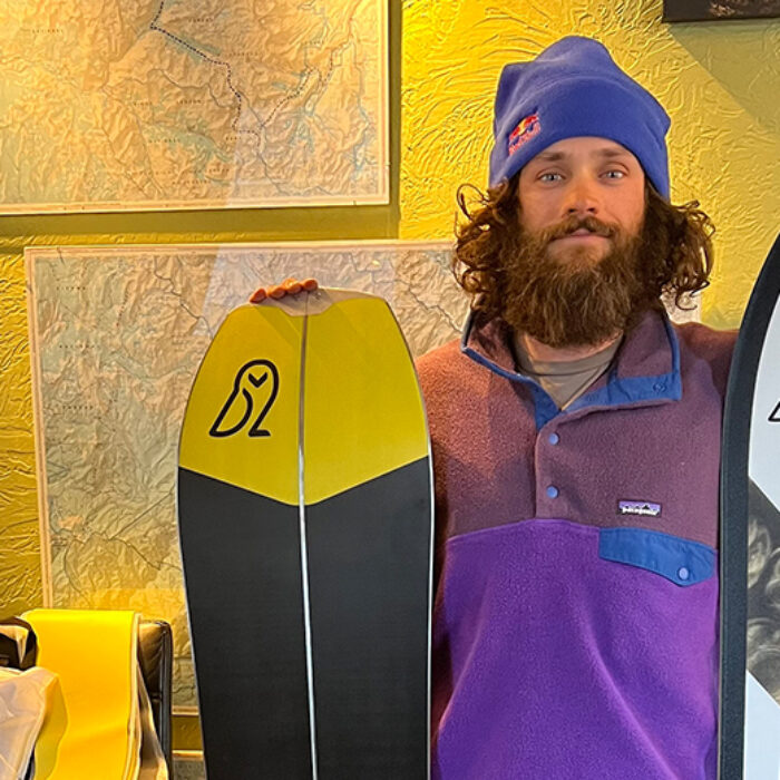 a bearded man holds two snowboards