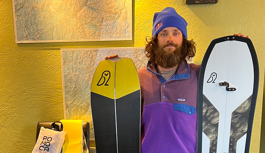 a bearded man holds two snowboards