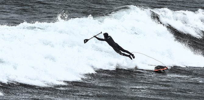 a stand up paddler diving for a wave with a leash attached