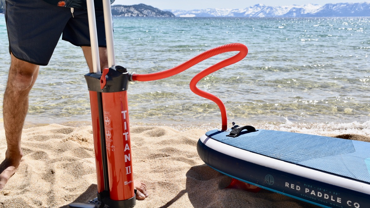a man inflating the red paddle ride msl inflatable paddle board with lake tahoe and mountains in the background
