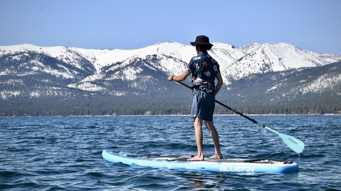 man paddling the bluefin cruise carbon inflatable paddle board on lake tahoe with snow capped mountains in background