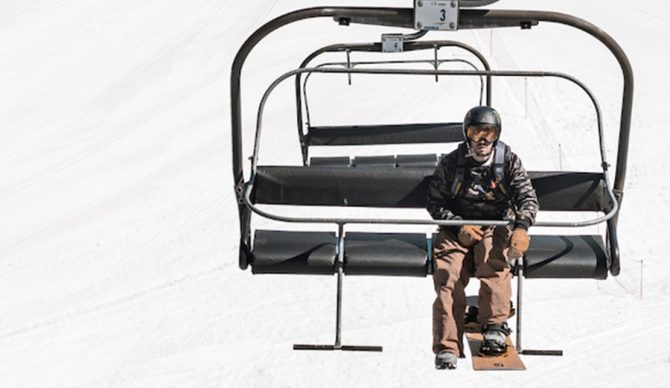 a man rides on a chairlift with his snowboard pointing forward. 