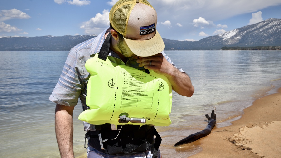 man inflating the mustang survival essentialist belt pack in front of lake tahoe