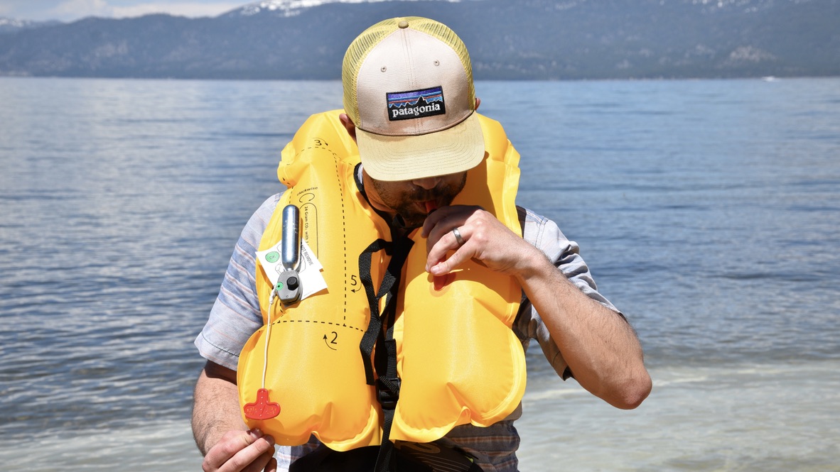 man inflating the nrs zephyr inflatable life jacket with lake tahoe in the background