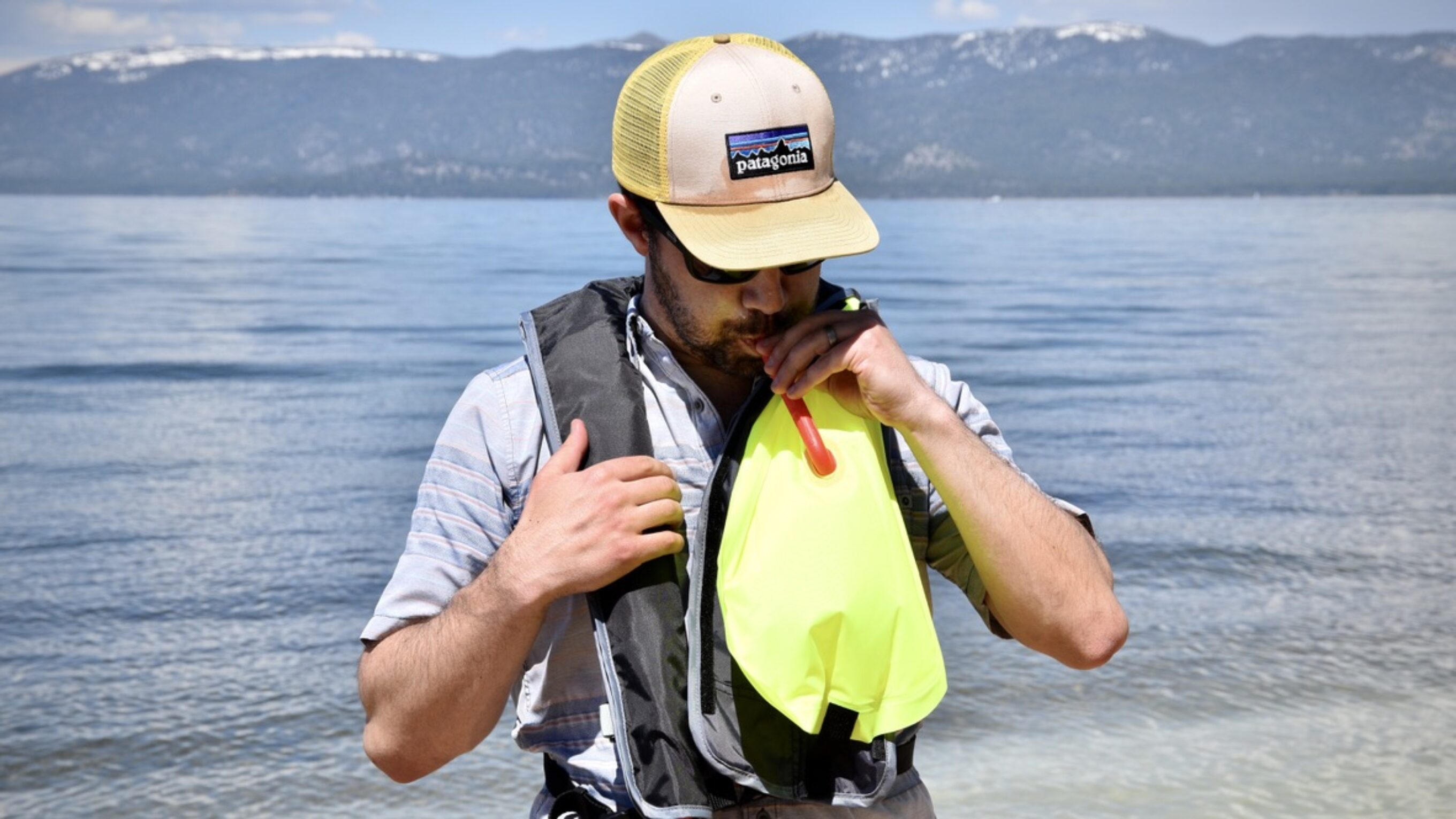 man inflating the BOTE inflatable vest life jacket in front of lake tahoe
