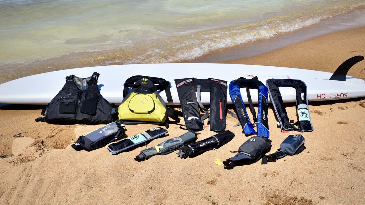 a lineup of 11 different life jackets set on a paddle board on a lake tahoe beach