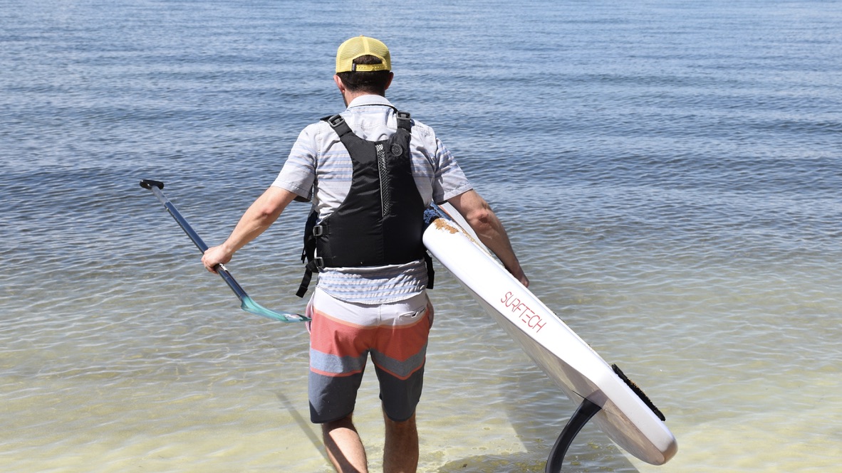 man walks on the beach into lake tahoe with a paddle board wearing the astral e-ronny life jacket
