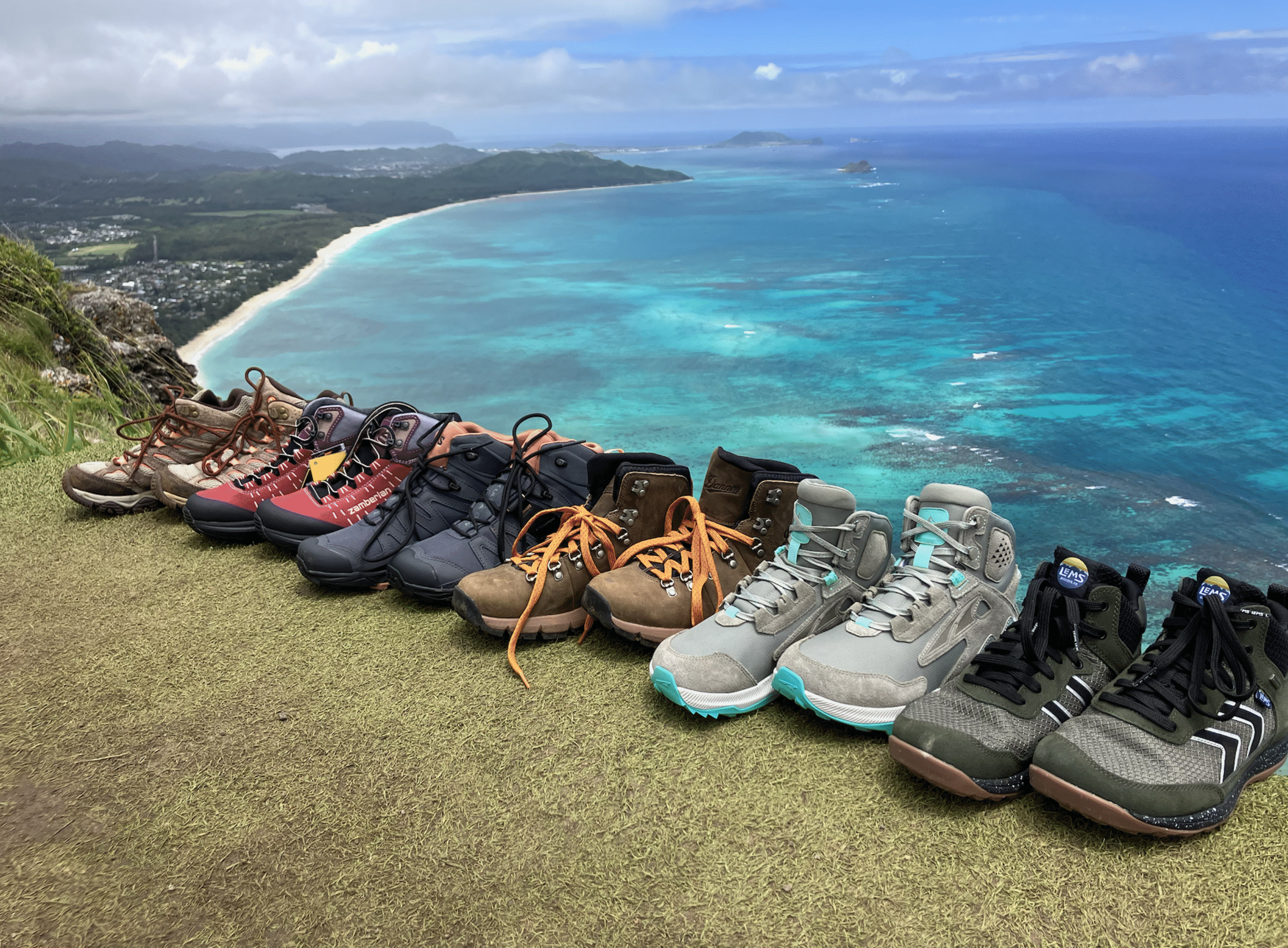 a bunch women's hiking boots lined up with the ocean in the background