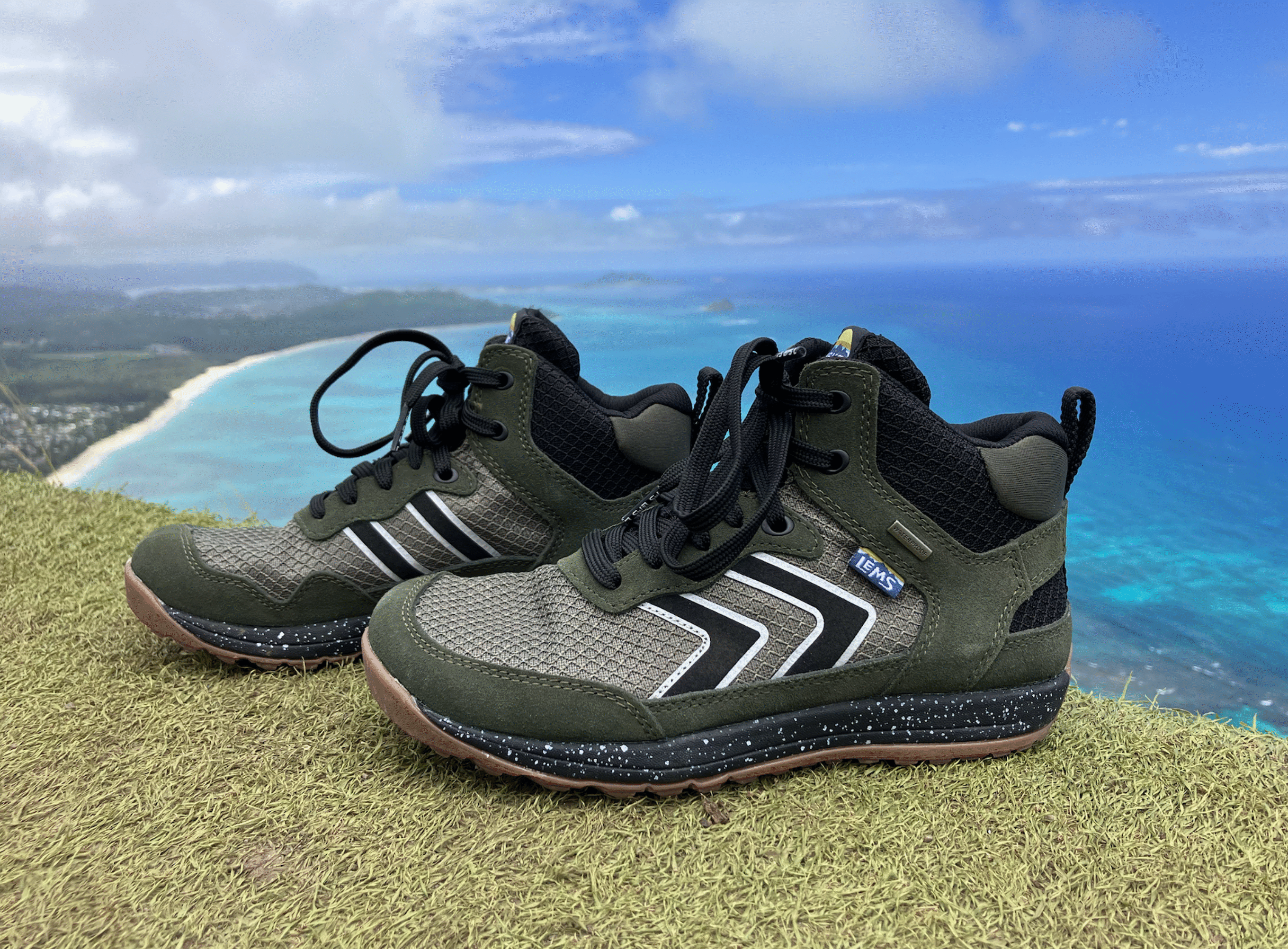 a close up of Lems Primal Pursuit Mid Waterproof hiking boots with the ocean in the background