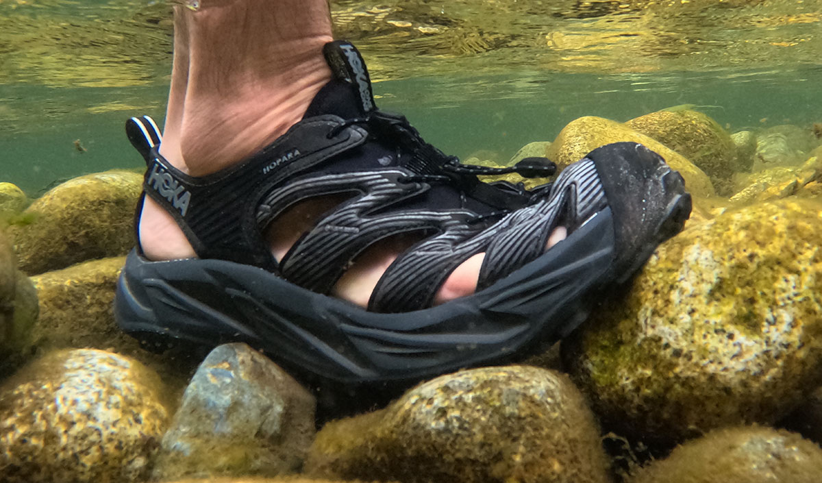 An underwater image of the Hoka Hopara water shoes on top of rocks in a creekbed.