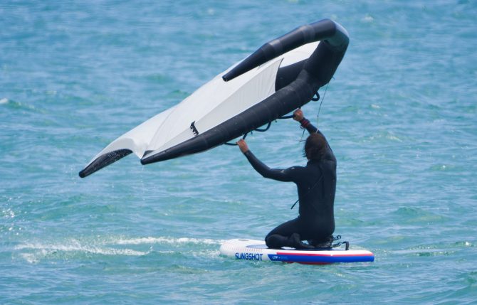 a man learning how to wing foil by starting on his knees on the slingshot ltf board in the water.
