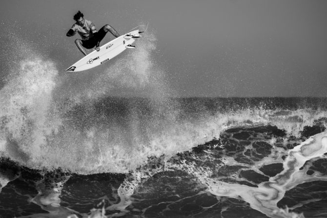 a surfer catching air high above a wave in france, shot in black and white