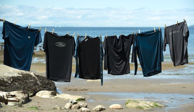six rash guards strung up on a clothesline at the beach for our review of the best men's rashguards.