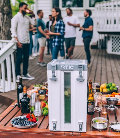 a patio party with a table of drinks and garnishes, with the 6 gallon rtic water cooler full of a mixed drink.