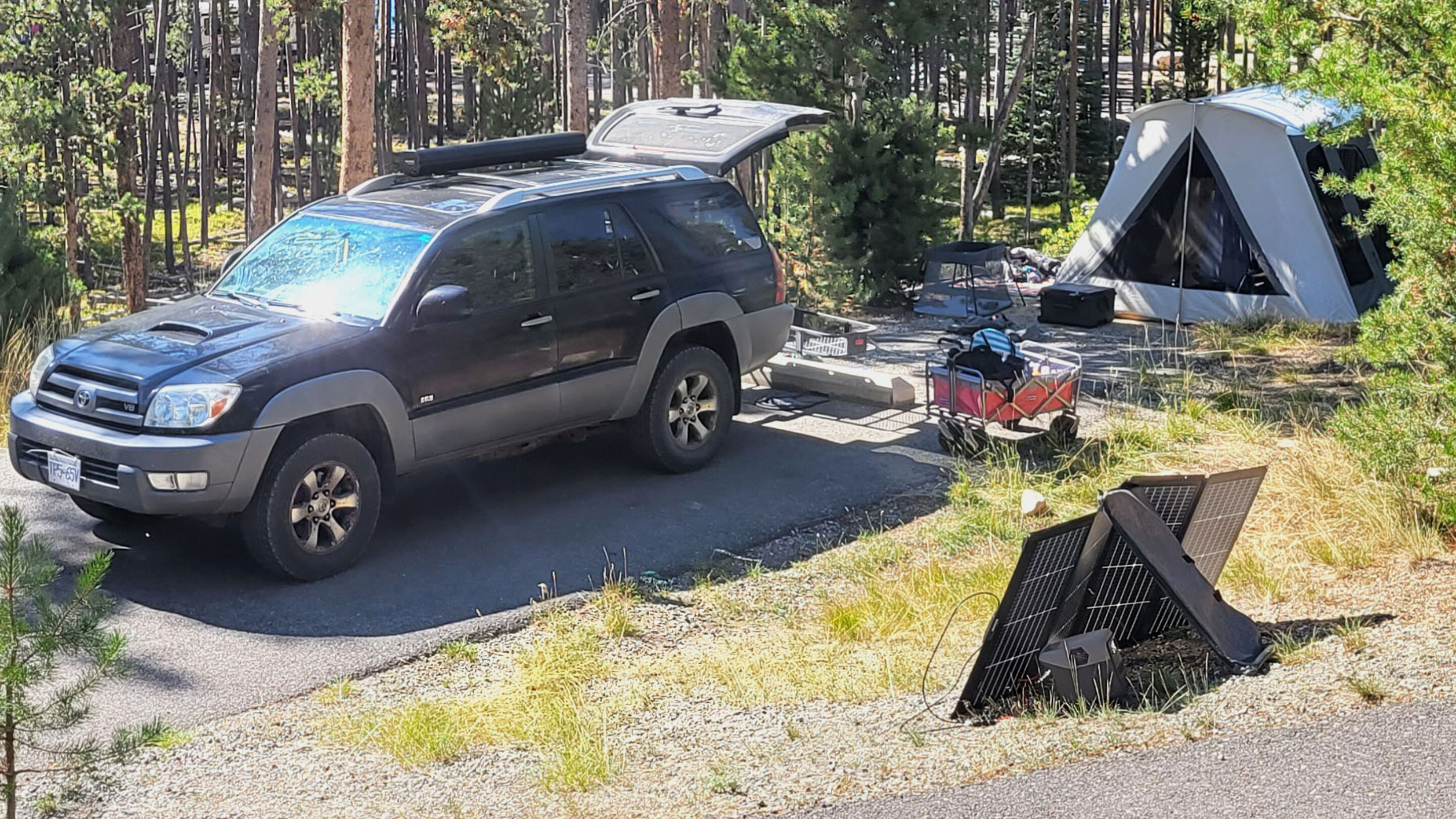 a campsite with a car unloading gear such as a tent, solar panel, wagon, and more for our review of the best car camping gear.