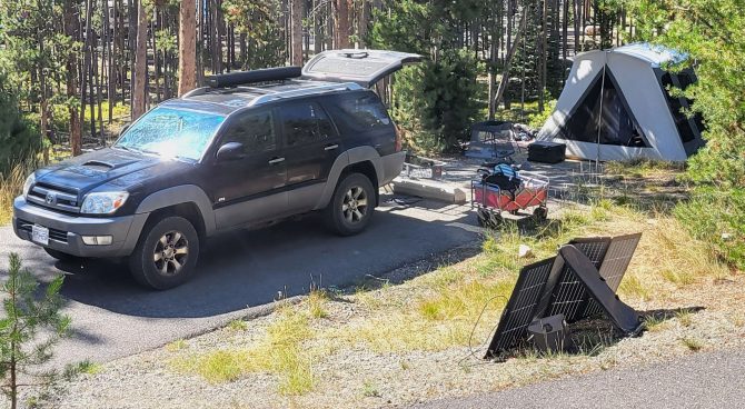 a campsite with a car unloading gear such as a tent, solar panel, wagon, and more for our review of the best car camping gear.
